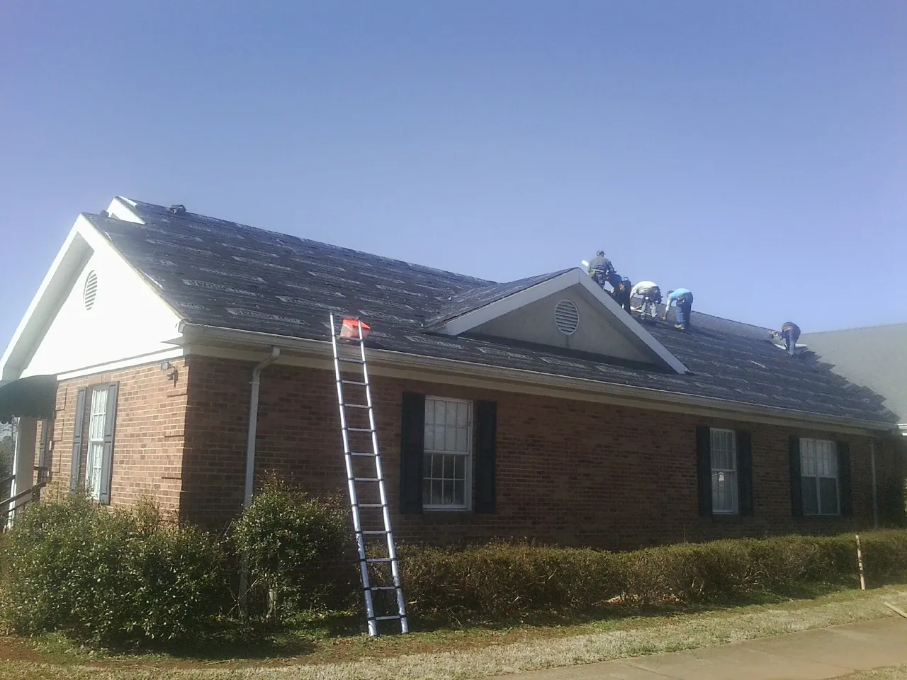 Crew tearing shingles off a brick ranch roof with a ladder set — Metal Roof Repair work by our crew in Lilly