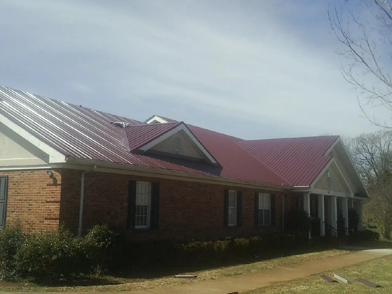 Red metal roof with gabled entries on a long brick building, from a Hail Damage Roof Repair job in Lilly