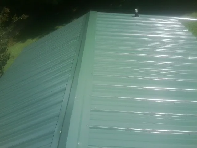 New green metal panels meeting at the ridge of a roof — Flat Roof Repair work by our crew in Lilly