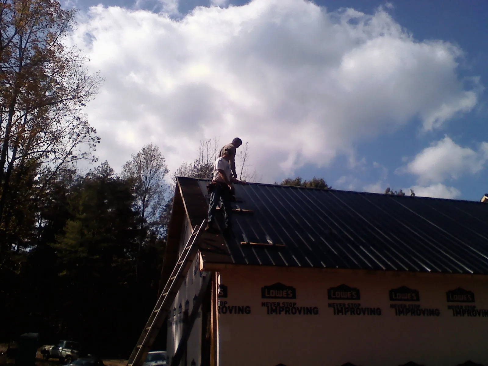 Roofer fastening dark metal panels high against a cloudy sky, from a Roof Inspection job in Lilly