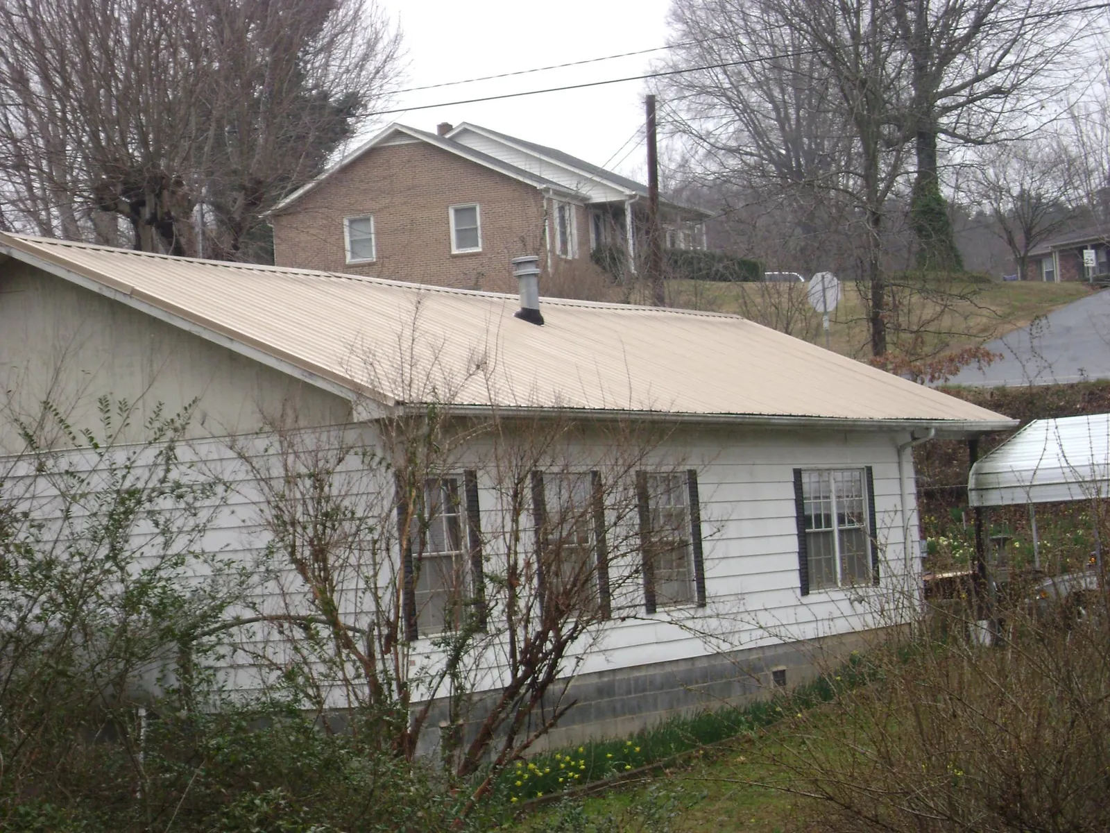 Tan metal roof on a white sided house set into a hillside — Commercial Roofing by Roofing Brothers in Lilly